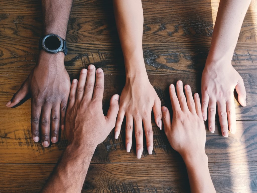 Five hands, palm facing down, representing students from diverse ethnic backgrounds