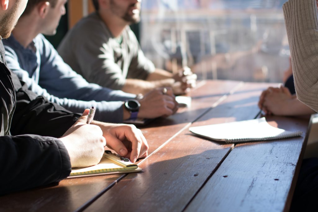 Students sitting at a table, ready to learn. Just a view of their hands ready to take notes.