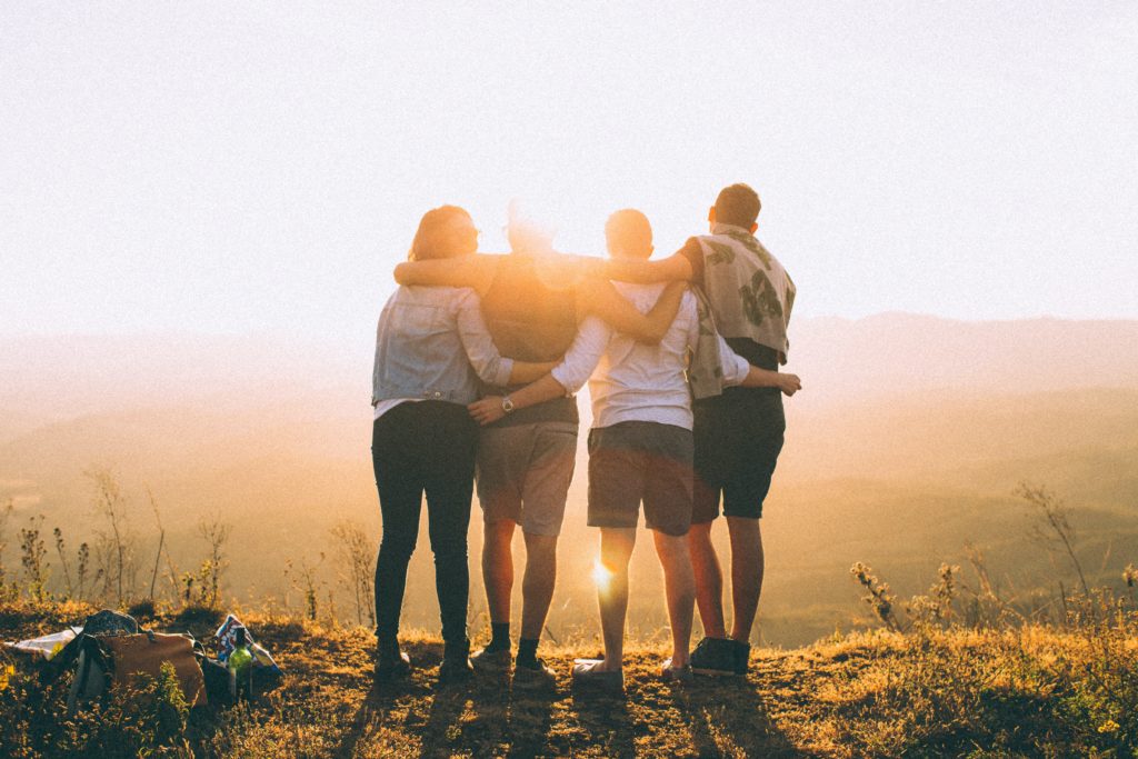 Four students standing on the brow of a hill, facing into the sunset, arms linked