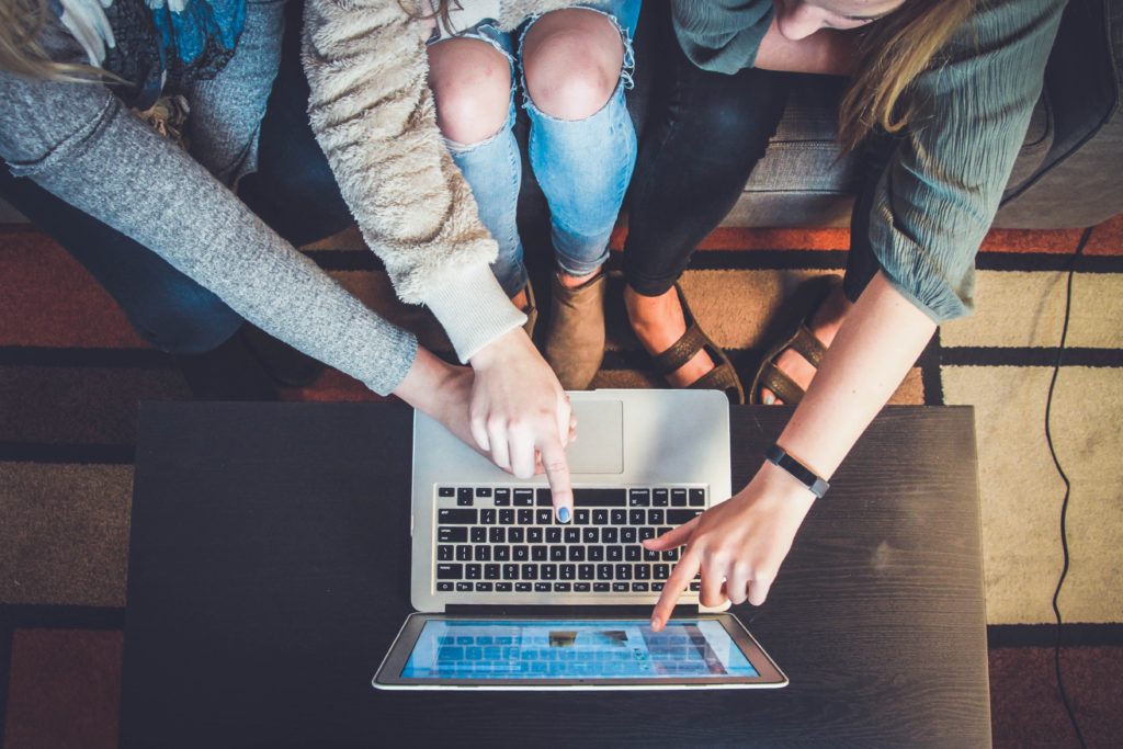 Picture of a laptop, with students pointing at the screen