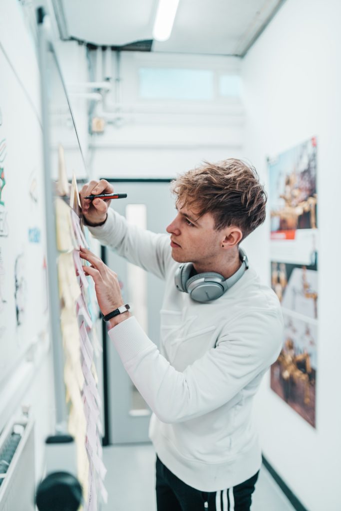 Student writing on a whiteboard, headphones round their neck