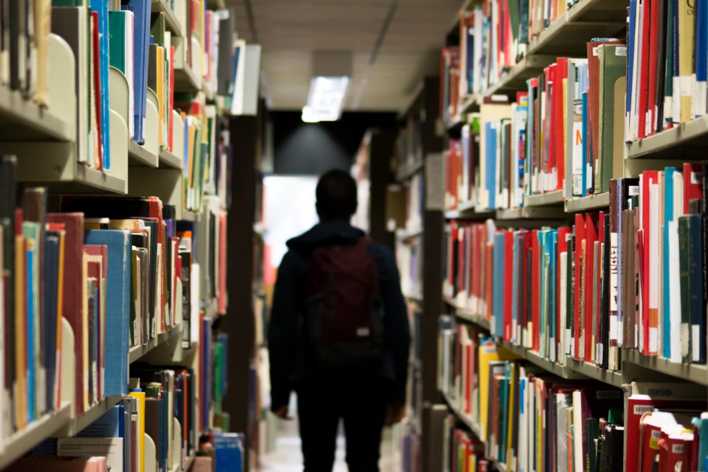 Student in shadow facing away form the camera, stanidng in an aisle in the university library