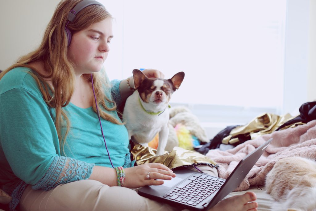 Female student working on her laptop, whilst her pet dog watches